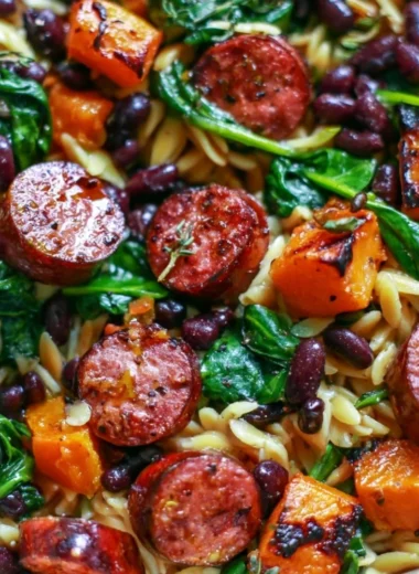 Butternut squash orzo dish with black beans, sausage, and spinach served in a bowl