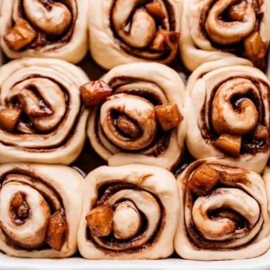 Cozy apple pie cinnamon rolls topped with icing on a rustic wooden table.