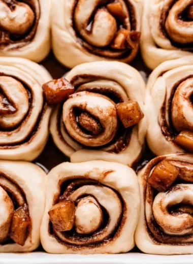 Cozy apple pie cinnamon rolls topped with icing on a rustic wooden table.